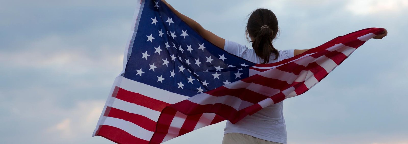 happy woman with flag of united states enjoying against the background of sunset sky. independence day concept